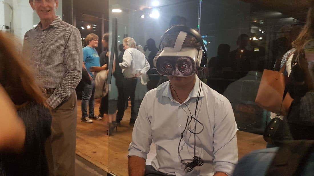 Man in a VR headset with gorilla eyes printed on the front, gallery crowd behind him