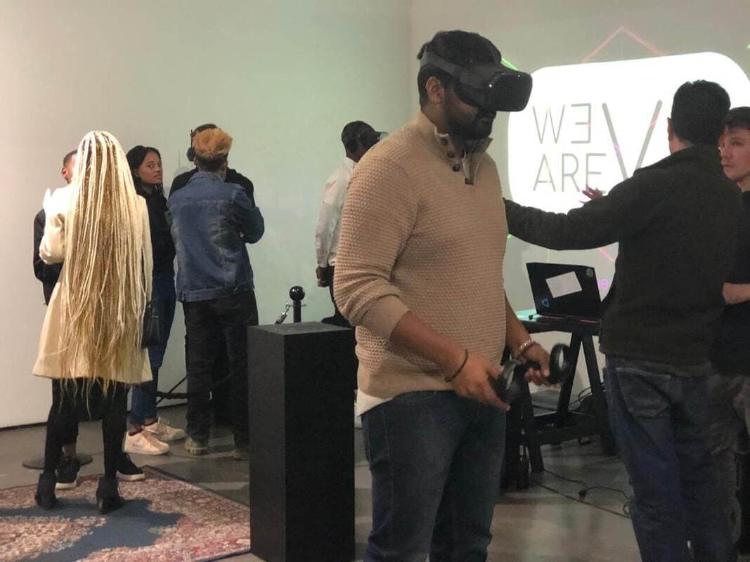 Man in a VR headset holding controllers, the WE ARE VR logo projected on the wall behind