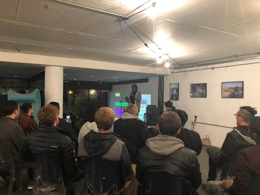 Speaker with a microphone in front of an agenda slide, audience seated in rows
